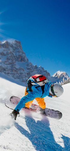 a man riding a snowboard down the side of a snow covered slope in front of a mountain