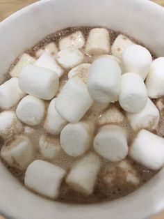 marshmallows in a white bowl on top of a wooden table next to a cup of hot chocolate