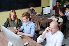 several people sitting at desks working on their laptops and talking on cell phones