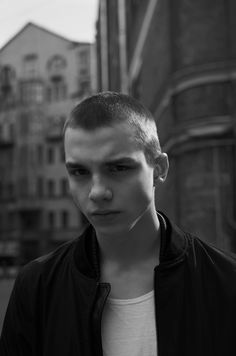 black and white photograph of a young man looking at the camera with buildings in the background