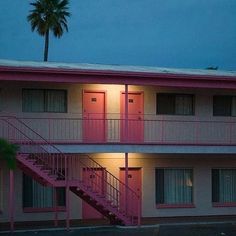 an apartment building with stairs leading up to the second floor and palm trees in front of it