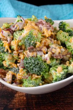 a white bowl filled with broccoli covered in cheese and other toppings on top of a wooden table