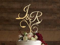 a wedding cake with the initials on it and flowers in front of a wooden wall