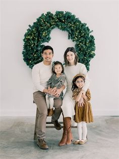 a family sitting on a bench in front of a christmas wreath with their two children