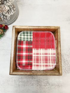 a red and white plaid dishcloth in a wooden tray with pine cones on the side