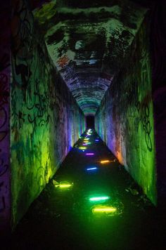 a long tunnel with graffiti on the walls and lights at the end that are brightly colored