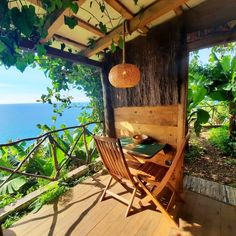 a wooden table and chairs under a tree on a deck overlooking the ocean with greenery