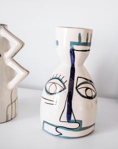 two vases with faces painted on them sitting next to each other in front of a white wall