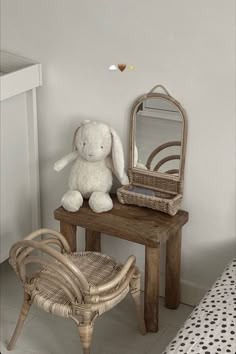 a white stuffed animal sitting on top of a wooden table next to a mirror and chair