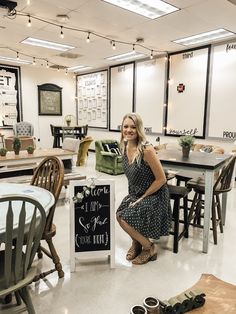 a woman sitting at a table in a room with chairs and signs on the floor