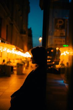 a person sitting on the side of a street next to a tall building at night