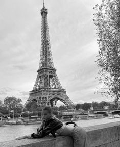 black and white photograph of a woman leaning against a wall in front of the eiffel tower