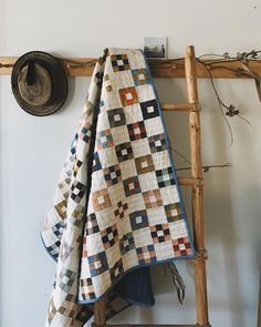 a quilt hanging on a wooden ladder next to a hat and wall mounted planter