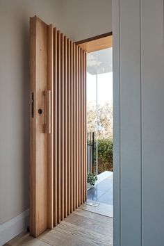 an open door with wooden slats on the outside and inside, in front of a white wall