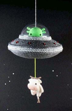 a stuffed animal hanging from a string in the shape of an alien ship on a black background