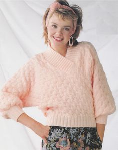 a woman wearing a pink sweater and flowered skirt with her hands on her hips