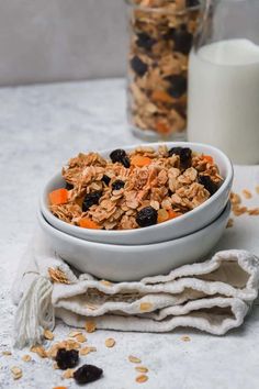 a bowl filled with granola and raisins next to a glass of milk