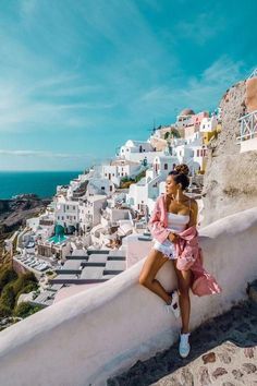 a woman sitting on top of a white building next to the ocean with buildings in the background