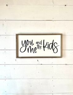 a sign that says you and me the kids hanging on a white wall with wood planks