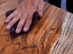 a person wiping up some wood with a cloth on top of the wooden table surface