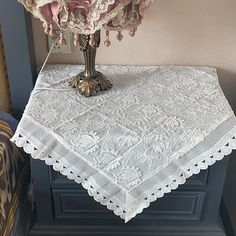 a table with a white doily on it and a vase filled with pink flowers