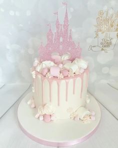 a pink and white cake with a castle on top that is dripping from the icing