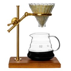 an old fashioned coffee pot and glass carafe on a wooden stand with a measuring cup