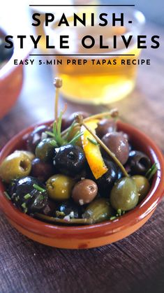 an orange bowl filled with olives on top of a wooden table