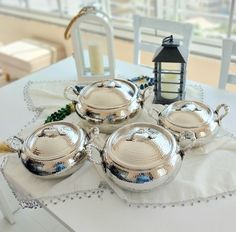 four silver pots and pans sitting on top of a table next to a lantern