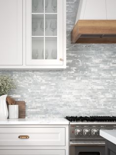 a kitchen with white cabinets and marble backsplash, an oven and counter tops