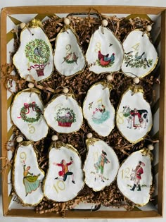 twelve decorated cookies in a box on top of some brown leaves and wood chips with christmas decorations