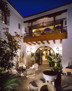 an outdoor patio with chairs and potted plants on the side walk, at night