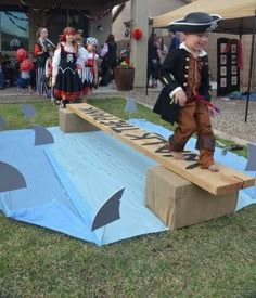 a young boy in pirate costume standing on a cardboard ramp with other children dressed as pirates