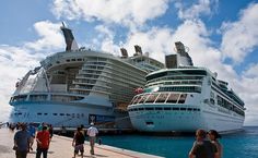 two cruise ships docked in the water with people standing around them and looking at them