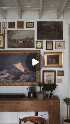 a living room filled with pictures and paintings on the wall above a wooden table topped with a potted plant