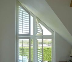 an open window with white shutters in a room next to a bed and desk