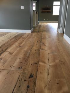 an empty room with hard wood floors and gray walls in the background is a hallway leading to another room