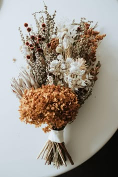 dried flowers are arranged on a white plate with brown and white stems in the center