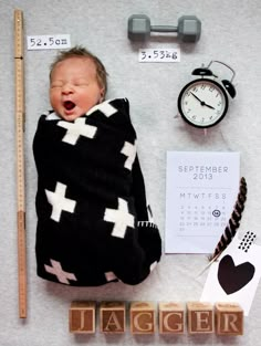 a baby wrapped up in a blanket next to some letters and a clock on the wall