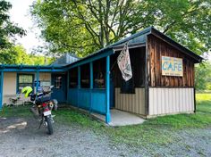 a motorcycle parked in front of a small building with a cafe sign on it's side