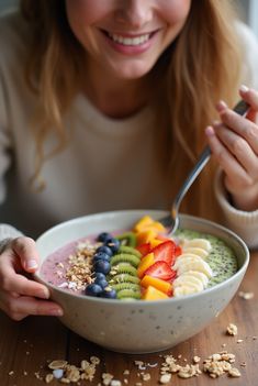 a woman eating a bowl of fruit with a spoon in her hand while smiling at the camera