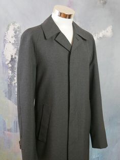 This charcoal gray overcoat is crafted from a high-quality wool-blend fabric, has a notch collar, and closes in the front with three concealed black buttons. The raglan style long sleeves feature a buttoned cuff strap, and the coat has two slanted storm pockets. The coat is lined in a black satin polyamid fabric (with one inner pocket), and a center vent in the back ensures complete ease of movement. Brand label: Oratop (Finland) Size: 44 US/UK Material: 45% Wool, 55% Polyester Condition: Near M Business Gray Pea Coat With Button Closure, Gray Pea Coat With Lapel Collar For Fall, Fitted Charcoal Outerwear For Winter, Classic Gray Pea Coat For Office, Classic Gray Outerwear With Lapel Collar, Gray Wool Outerwear For Work, Gray Lapel Collar Pea Coat For Fall, Modern Fall Outerwear With Suit Collar, Gray Business Pea Coat With Button Closure