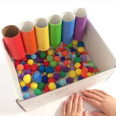 a box filled with lots of different colored pom - poms next to a person's hand