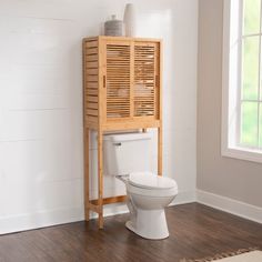 a bathroom with a wooden cabinet and toilet in it's corner next to a window