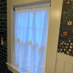 a bathroom window with white curtains and black tile wall behind it, next to a toilet