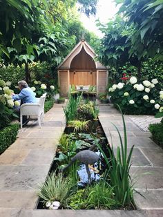 a woman sitting on a chair next to a small pond in the middle of a garden