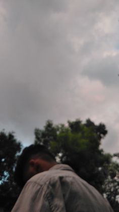 a man is flying a kite high in the air with trees behind him and clouds overhead