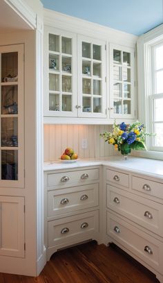 a kitchen with white cabinetry and wooden flooring next to a vase filled with flowers