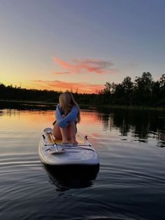 a woman sitting on top of a paddle boat in the middle of water at sunset