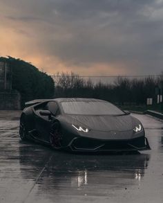 a black sports car is parked on the wet pavement in front of a building with dark clouds